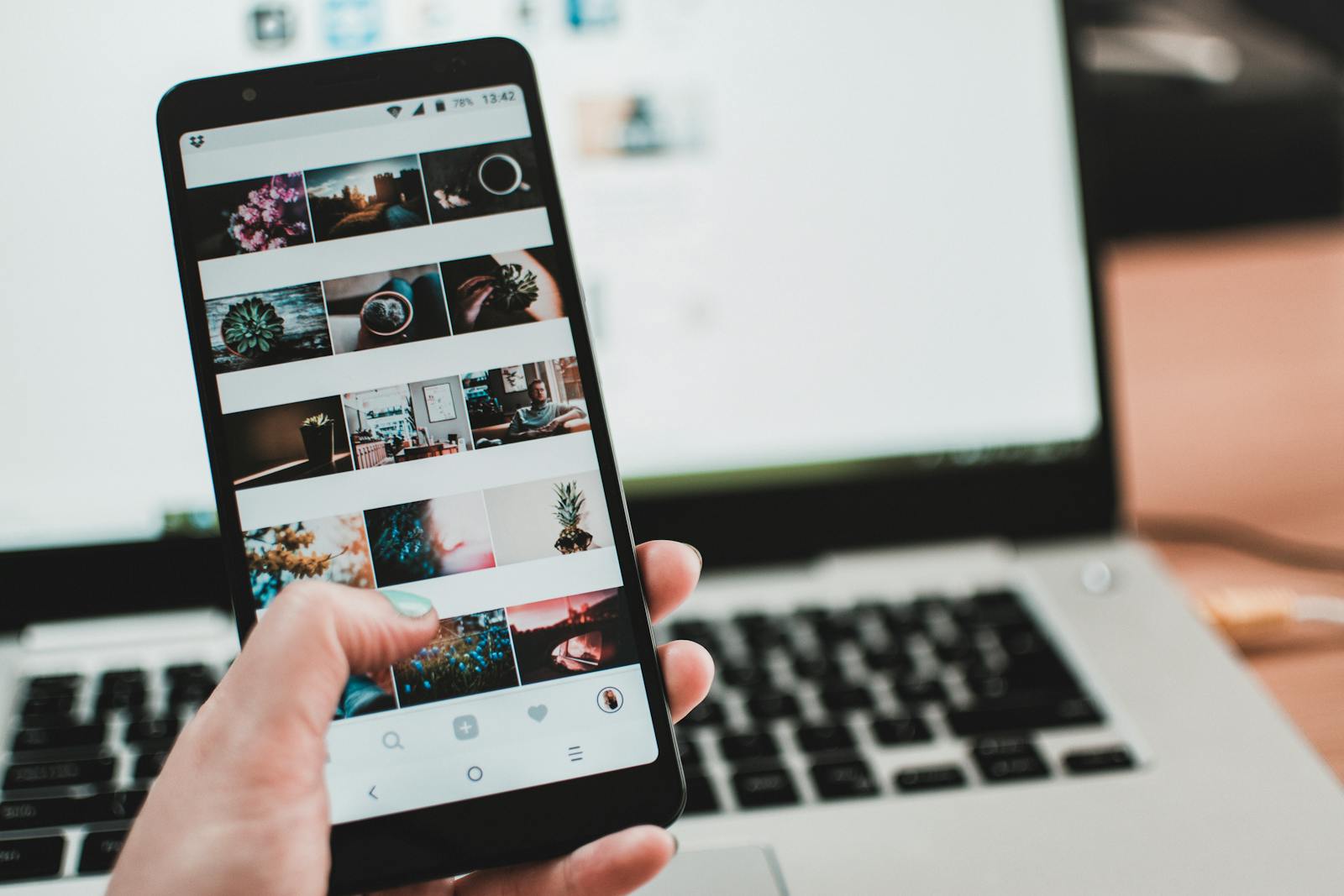 A person uses a smartphone to browse social media in front of a laptop, emphasizing modern technology and lifestyle.